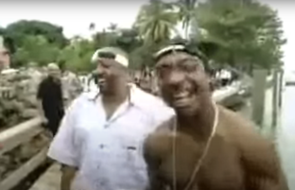 Ja Rule and a friend smiling and walking by a crowd, one wearing a bandana and sunglasses, the other in a casual shirt