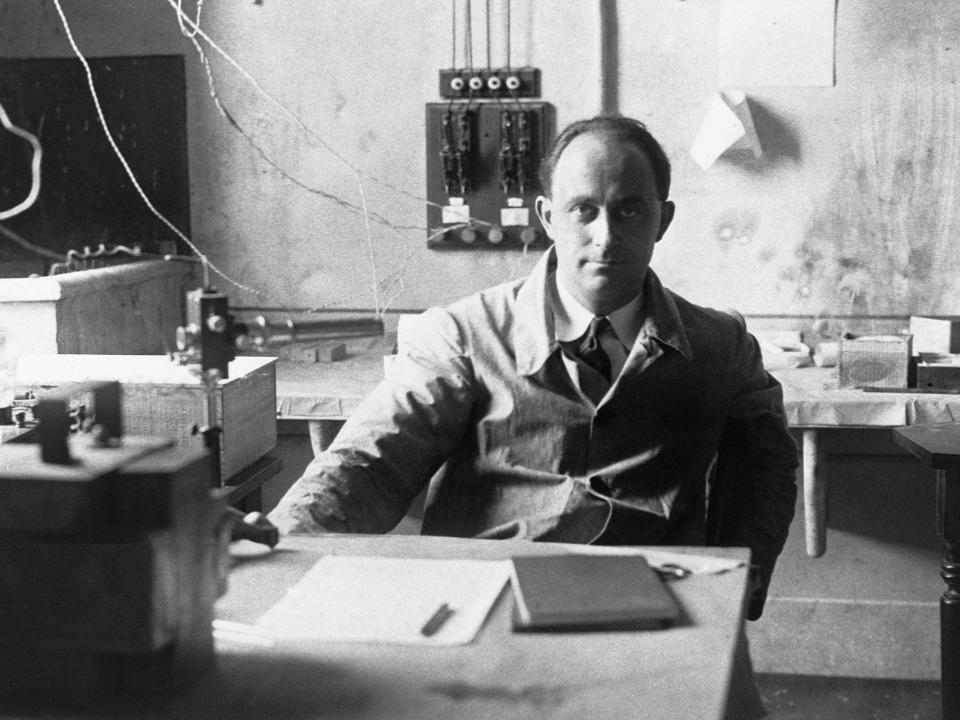 black and white photo of enrico fermi wearing a coat sitting at a desk in a laboratory