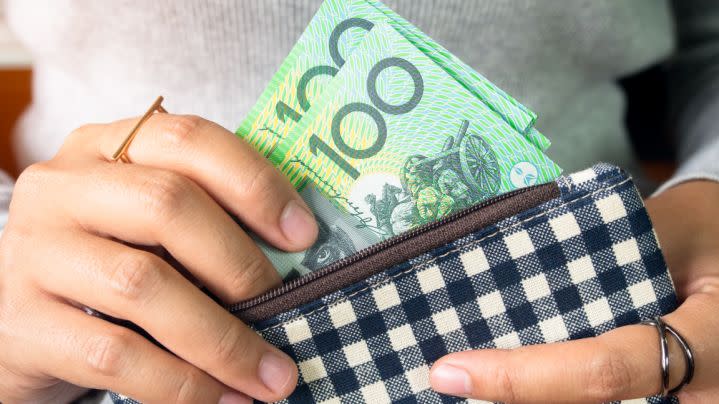 Woman's hand puts Australian $100 bills in a purse.