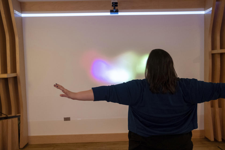 Emily Hollenbeck, a deep brain stimulation therapy patient, demonstrates how she makes circles in the air with her arms that are interpreted and projected as light on an interactive wall at Mount Sinai’s “Q-Lab” in New York on Dec. 20, 2023. Researchers use various methods to collect data as patients recover. Like many other patients, she moves her arms faster now that she’s doing better. (AP Photo/Mary Conlon)