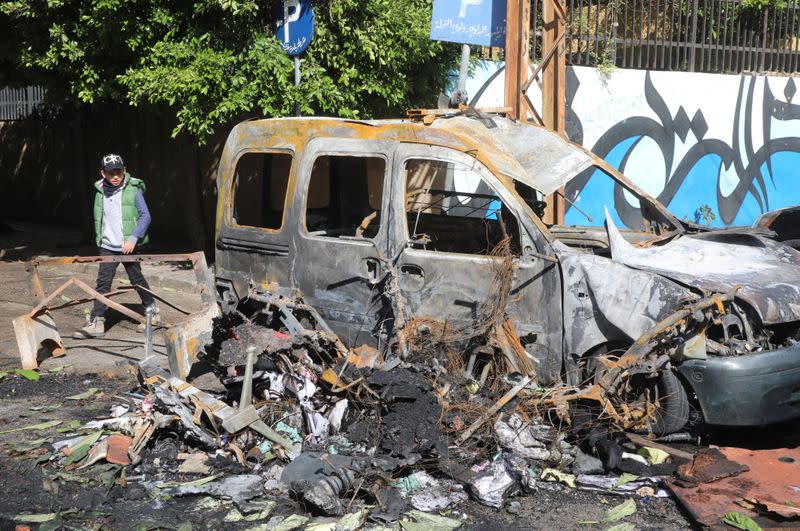 A boy walks near a burnt vehicle, in the aftermath of protests against the lockdown and worsening economic conditions, amid the spread of the coronavirus disease (COVID-19), in Tripoli