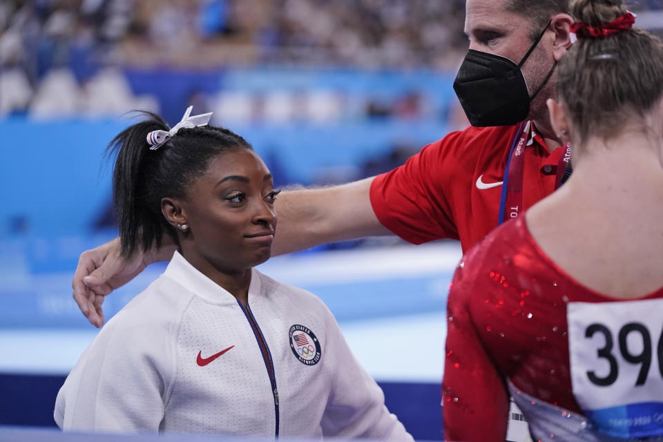 Coach Laurent Landi comforts Simone Biles, of the United States, after she exited the team final with apparent injury, at the 2020 Summer Olympics, Tuesday, July 27, 2021, in Tokyo. The 24-year-old reigning Olympic gymnastics champion Biles huddled with a trainer after landing her vault. She then exited the competition floor with the team doctor. (AP Photo/Gregory Bull)