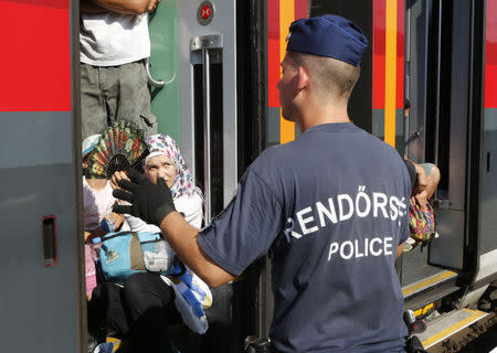 A Hungarian police officer gestures to travelers as a train heading for Austria, with migrants on board, is stopped for checks at a border station in Hegyeshalom, Hungary, August 31, 2015. REUTERS/Heinz-Peter Bader