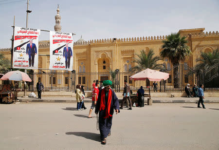 People walk in front of posters of Egypt's President Abdel Fattah al-Sisi in front of an old mosque during the preparations for tomorrow's presidential election in Cairo, Egypt March 25, 2018. REUTERS/Ammar Awad