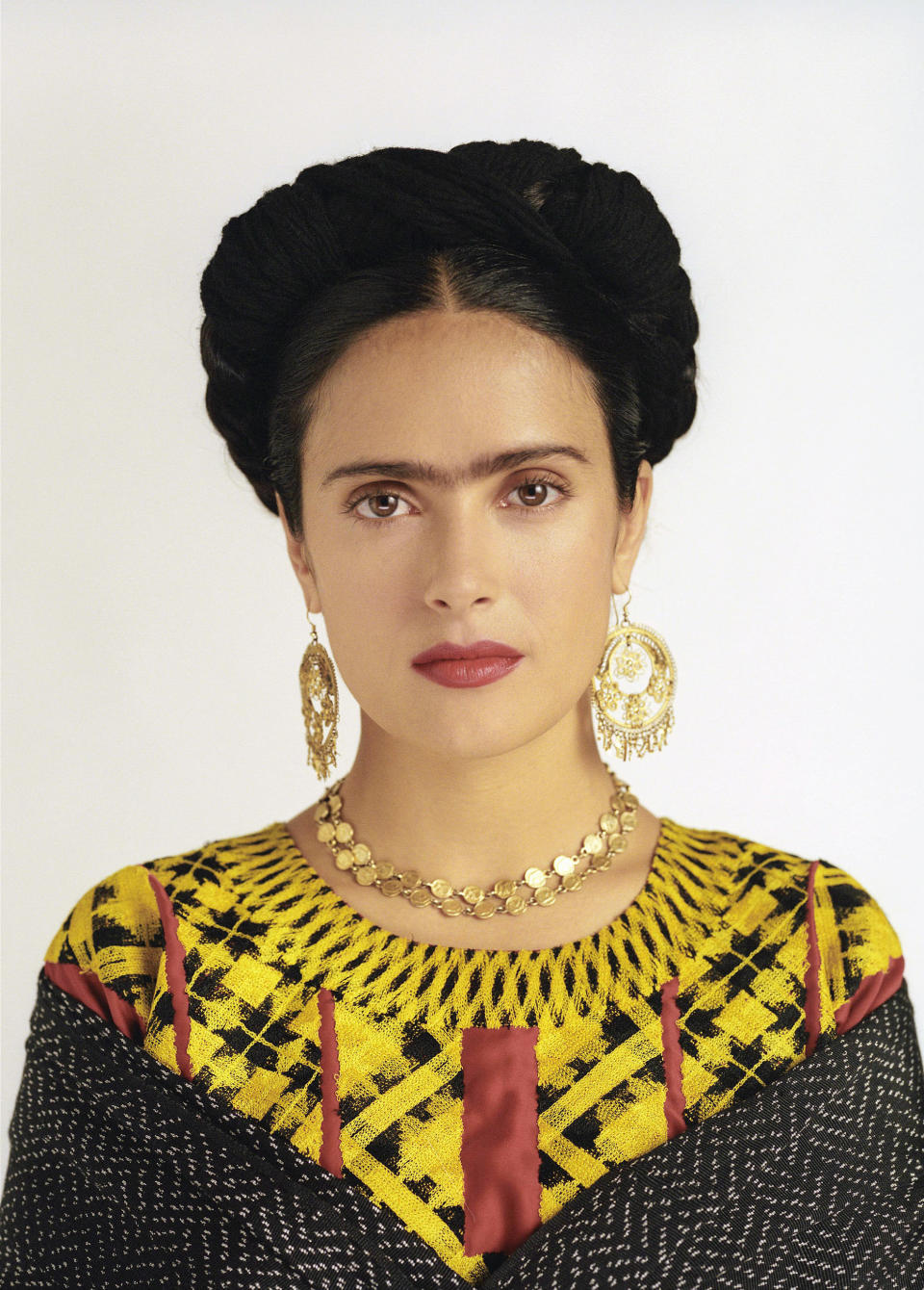 Hayek with a unibrow, wearing colorful gown, and gold jewelry in "Frida"