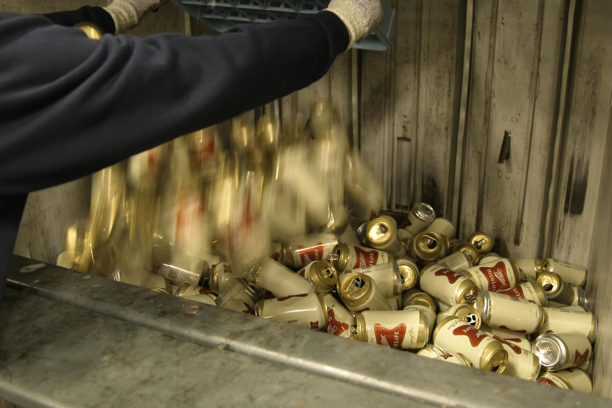 In this image provide by Comite Champagne, a worker dumps empty cans of Miller High Life beer into a machine to be crushed at the Westlandia plant in Ypres, Belgium, Monday, April 17, 2023. Belgian customs have destroyed more than 2,000 cans of Miller High Life advertised as the ″Champagne of beers” at the request of houses and growers of the bubbly beverage. (Comite Champagne via AP)