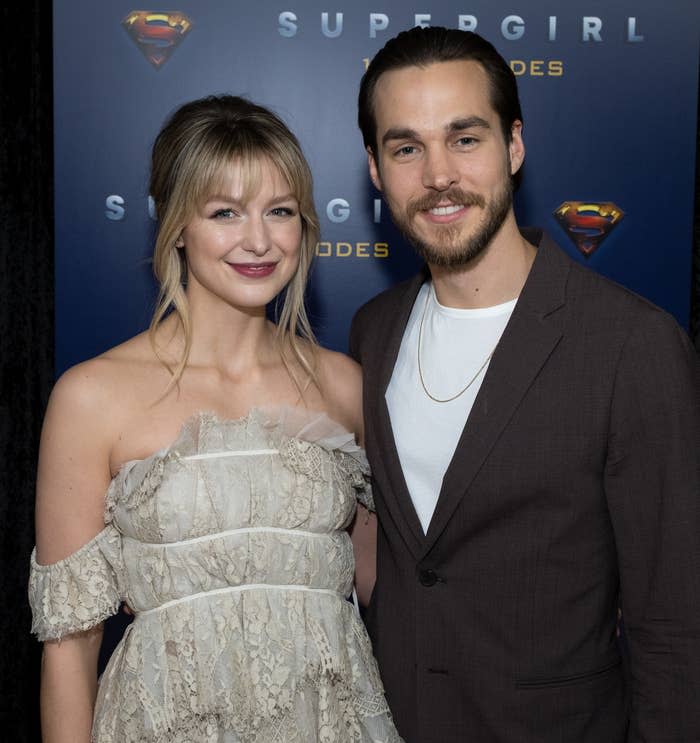 Two actors from Supergirl TV show posing, one in a lace dress and the other in a suit without a tie