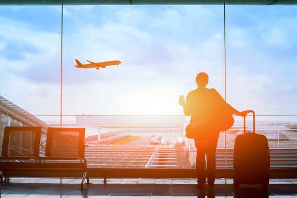 A woman watches from an airport as a plane takes off.