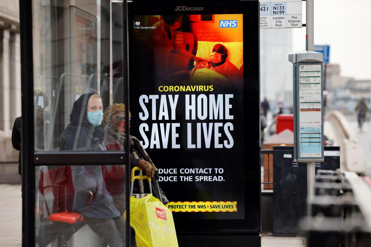 A woman wearing a face mask as a precautionary measure against COVID-19, waits in a busstop with NHS signage on keeping safe, at London Bridge in London on January 15, 2021, during the third coronavirus lockdown. - Britain's economy slumped 2.6 percent in November on coronavirus restrictions, official data showed January 15, 2021, stoking fears that the current virus lockdown could spark a double-dip recession. (Photo by Tolga Akmen / AFP) (Photo by TOLGA AKMEN/AFP via Getty Images)