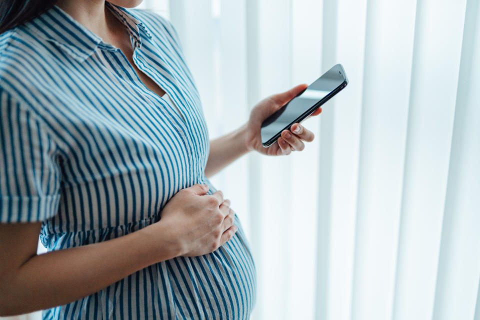 Midsection of pregnant woman using pregnancy tracker app on smartphone to see the development of her baby. Telehealth, fertility and family concept.