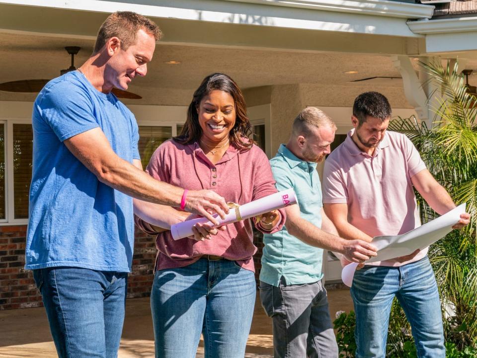 Four people look at floorplans outside of a home.