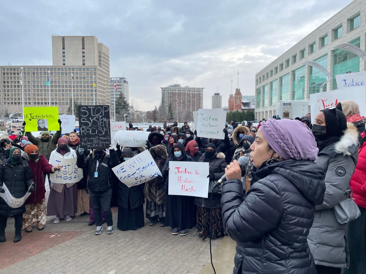 Khadija El Hilali speaks into a microphone at a vigil for 23-year-old Hodan Hashi on Saturday. El Hilali said the purpose of the vigil was not only to grieve for Hashi, who died in a fight at a Saskatchewan nightclub, but also to demand justice. (Avanthika Anand/CBC - image credit)