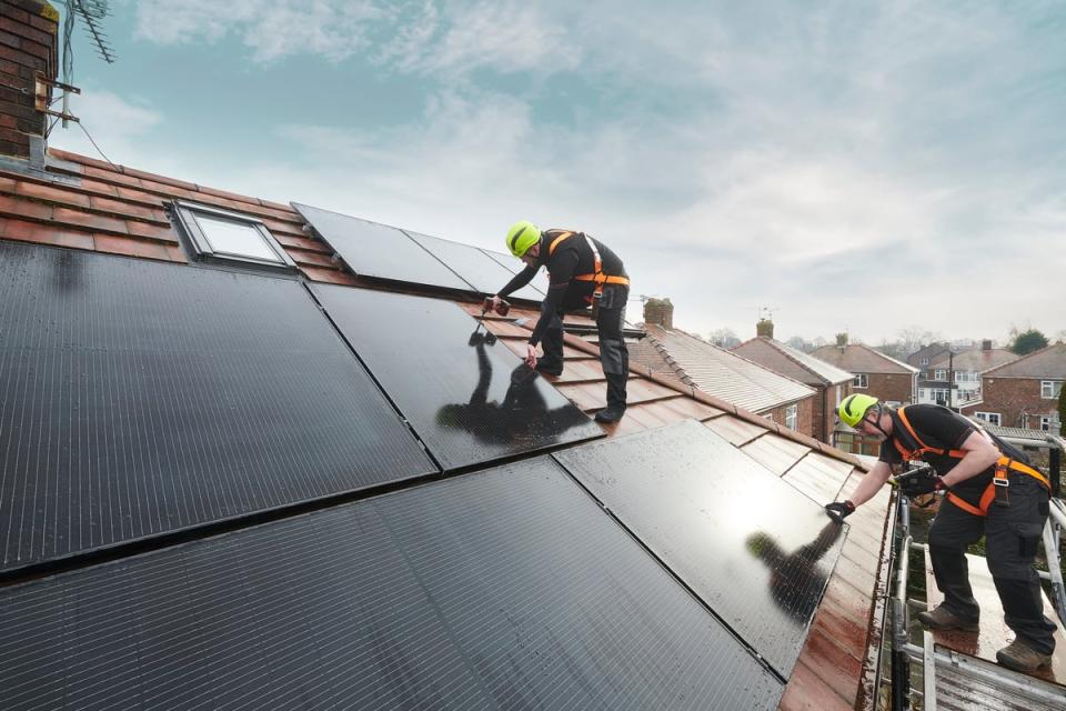 Two workers install rooftop solar panels in a residential setting. 