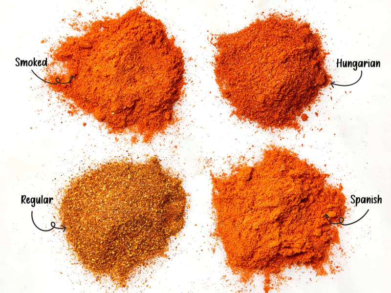 4 different types of paprika piled on a surface: smoked, hungarian, regular, and Spanish