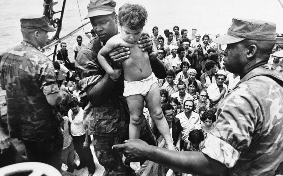 FILE- In this May 10, 1980, file photo, a U.S. Marine helps a young Cuban child off a refugee boat in Key West, Fla. Throughout history, the United States has used all sorts of physical or mental exams for immigrants seeking just to get into the country outside of becoming a citizen. (AP Photo/Fernando Yovera, File)