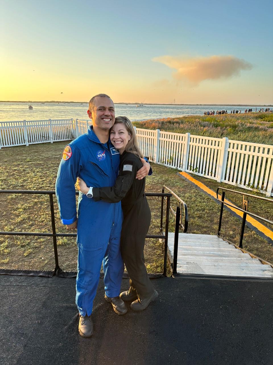 Anil and Anna Menon hugging on the beach in their respective NASA and SpaceX astronaut jumpsuits.