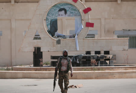 A Kurdish fighter from the People's Protection Units (YPG) carries his weapon as he walks at the faculty of economics where a defaced picture of Syrian President Bashar al-Assad is seen in the background, in the Ghwairan neighborhood of Hasaka, Syria, August 22, 2016. REUTERS/Rodi Said