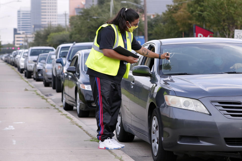 Volunteer Sharely Gomez marks the windshield after taking information from clients in their cars as they wait in line in before the food distribution begins at the West Houston Assistance Ministries Wednesday, Oct. 14, 2020, in Houston. Each car is marked to denote if there are kids or pets, gluten allergies and other special hygiene needs. WHAM is one of the many distribution points that gets food from the Houston Food Bank and other retail contributors to those in need around the 18 counties served by the food bank. (AP Photo/Michael Wyke)