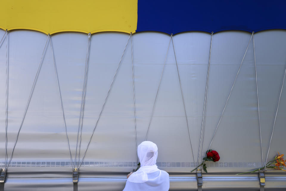 A woman places a flower in Visoko, Bosnia, Sunday, July 9, 2023 on a truck carrying 30 coffins with remains of the recently identified victims of the 1995 Srebrenica genocide. So far, the remains of more than 6,600 people have been found and buried at a vast and ever-expanding memorial cemetery in Potocari, outside Srebrenica. (AP Photo/Armin Durgut)