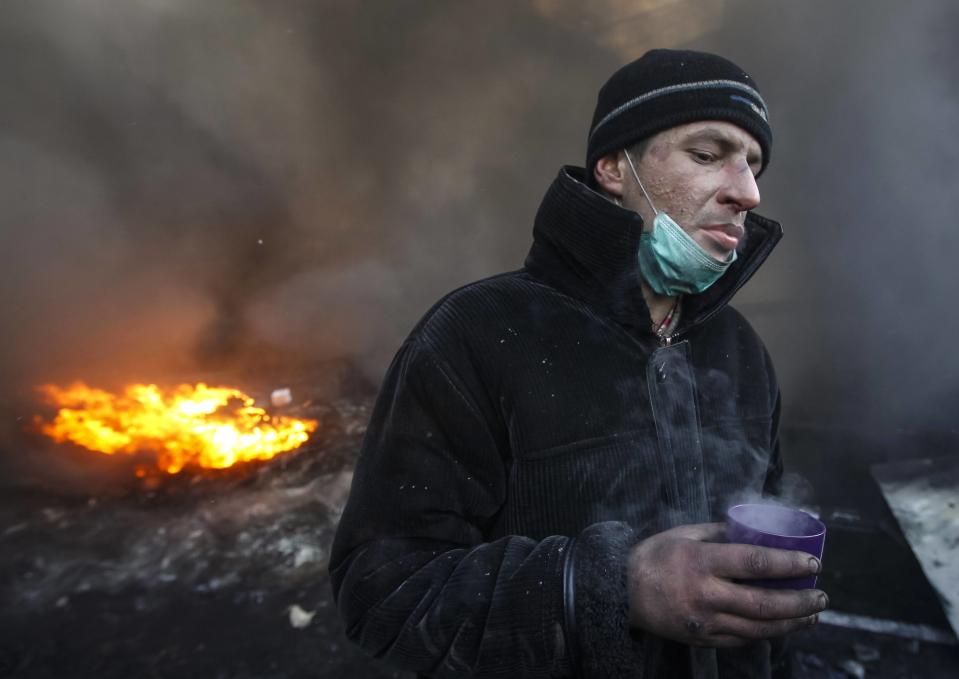 A pro-European integration protester drinks near burning tyres at the site of clashes with riot police in Kiev