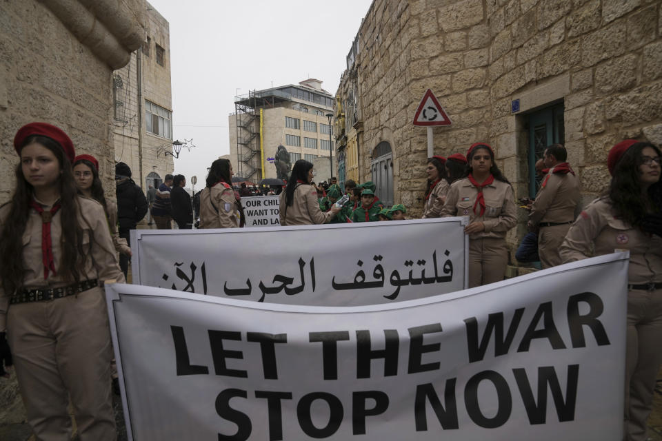 Palestinian scouts hold signs in solidarity with Palestinians in the Gaza Strip calling to end the Israel-Hamas war, near the Church of the Nativity, traditionally believed to be the birthplace of Jesus, on Christmas Eve in the West Bank city of Bethlehem, Sunday, Dec. 24, 2023. Bethlehem is having a subdued Christmas after officials in Jesus' traditional birthplace decided to forgo celebrations due to the Israel-Hamas war. (AP Photo/Mahmoud Illean)