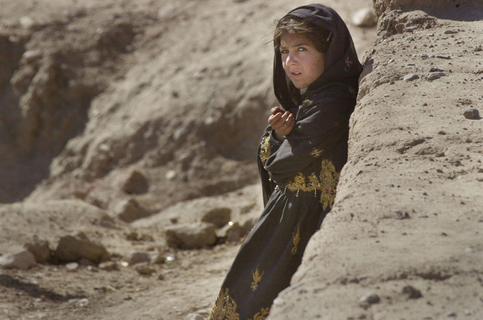 <p>An Afghan girl peers out from behind a wall at passing U.S. Marines<br> driving inside light armored vehicles down Route 4 outside the Kandahar airport, Dec. 27, 2001. (Photo: Earnie Grafton/Reuters) </p>