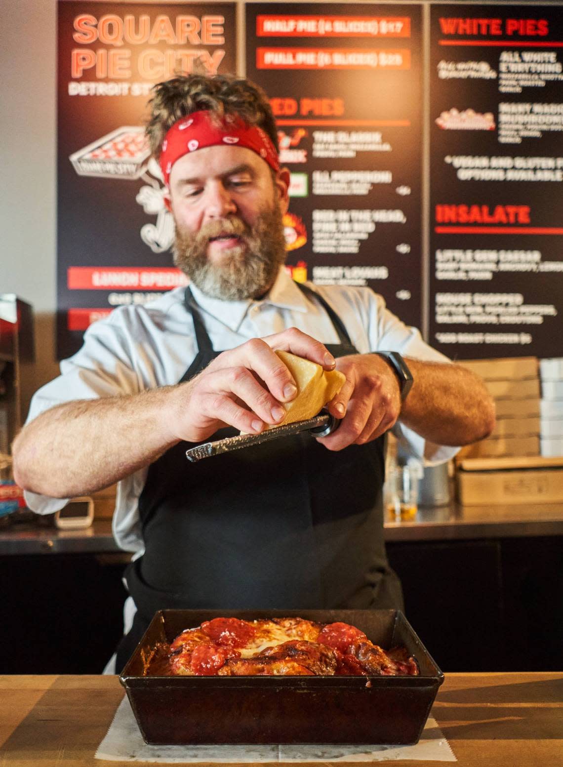 Chef Jeremiah Bullfrog grates cheese over a pizza at Square Pie City.