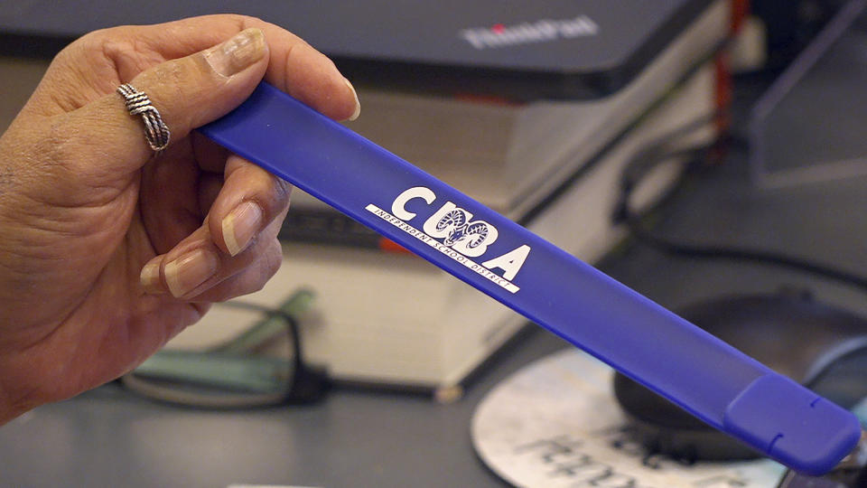 Veronica Madrid, administrative assistant at Cuba High School shows a slap bracelet USB drive loaded with assignments Oct. 19, 2020, outside Cuba, New Mexico. The closing of classrooms and the switch to remote learning because of the coronavirus outbreak have left Castillo and other students in this school district on the sparsely populated fringe of the Navajo Nation in New Mexico profoundly isolated, cut off from other people — and, in many cases, the grid — by sheer distance. (AP Photo/Cedar Attanasio)