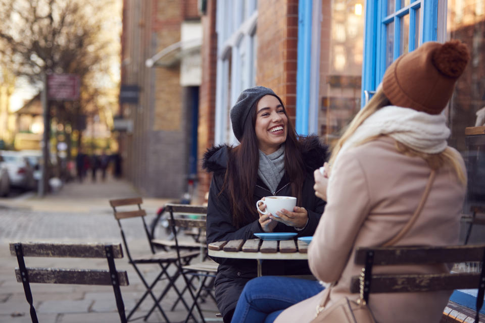 Two Female Friends Meeting Sitting Outside Coffee Shop On City High Street