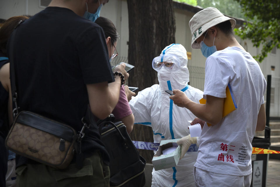 A worker in a protective suit checks the smartphone health app data of people at a COVID-19 testing site for those who were potentially exposed to the coronavirus outbreak at a wholesale food market in Beijing, Wednesday, June 17, 2020. As the number of cases of COVID-19 in Beijing climbed in recent days following an outbreak linked to a wholesale food market, officials announced they had identified hundreds of thousands of people who needed to be tested for the coronavirus. (AP Photo/Mark Schiefelbein)