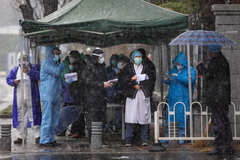 Medical staff and government workers wait for patients' arrival outside a tumor hospital which was just designated to take in critical COVID-19 patients in Wuhan in central China's Hubei province Saturday, Feb. 15, 2020.