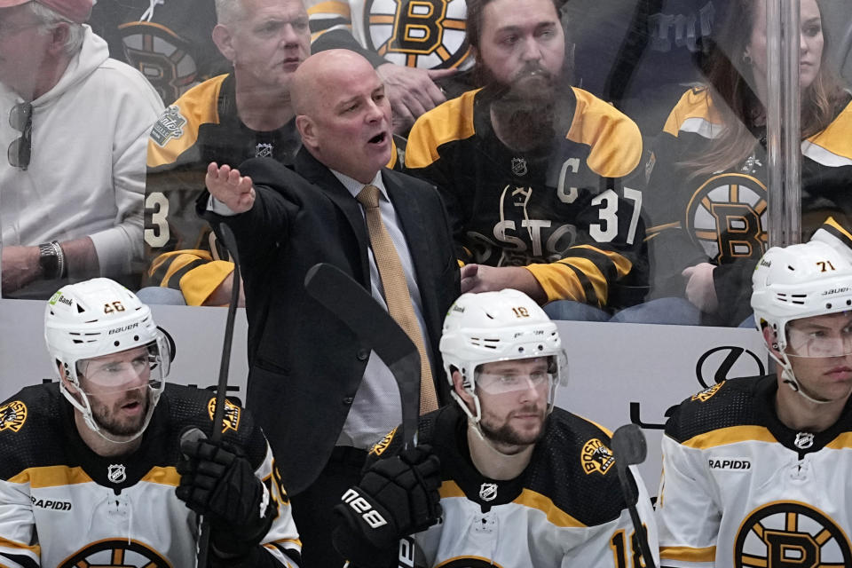 Boston Bruins head coach Jim Montgomery, center standing, talks to an official standing nearby in the third period of an NHL hockey game against the Dallas Stars, Tuesday, Feb. 14, 2023, in Dallas. (AP Photo/Tony Gutierrez)