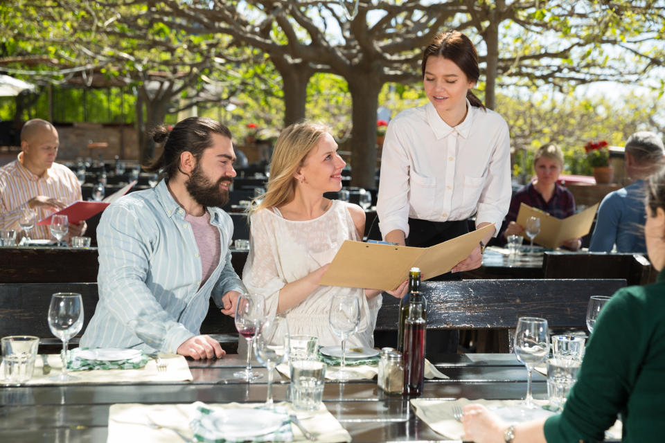 Two people sitting at a table and talking to a waiter about an item on the menu