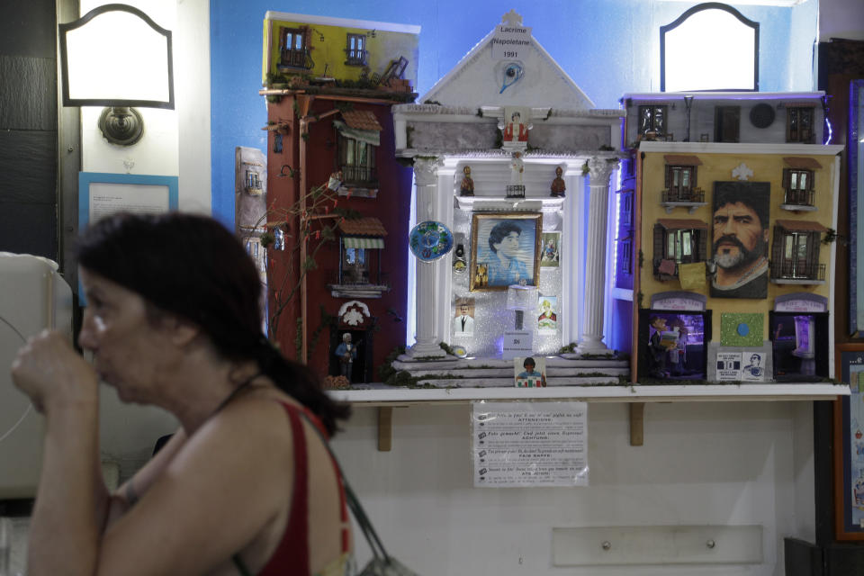 A woman sips a coffee next to a makeshift shrine of soccer legend and former Napoli player Diego Armando Maradona inside the Bar Nilo in downtown Naples, Italy, Wednesday, Sept. 18, 2019. Maradona achieved some of his most memorable exploits and in Naples is still revered with god-like status. (AP Photo/Gregorio Borgia)