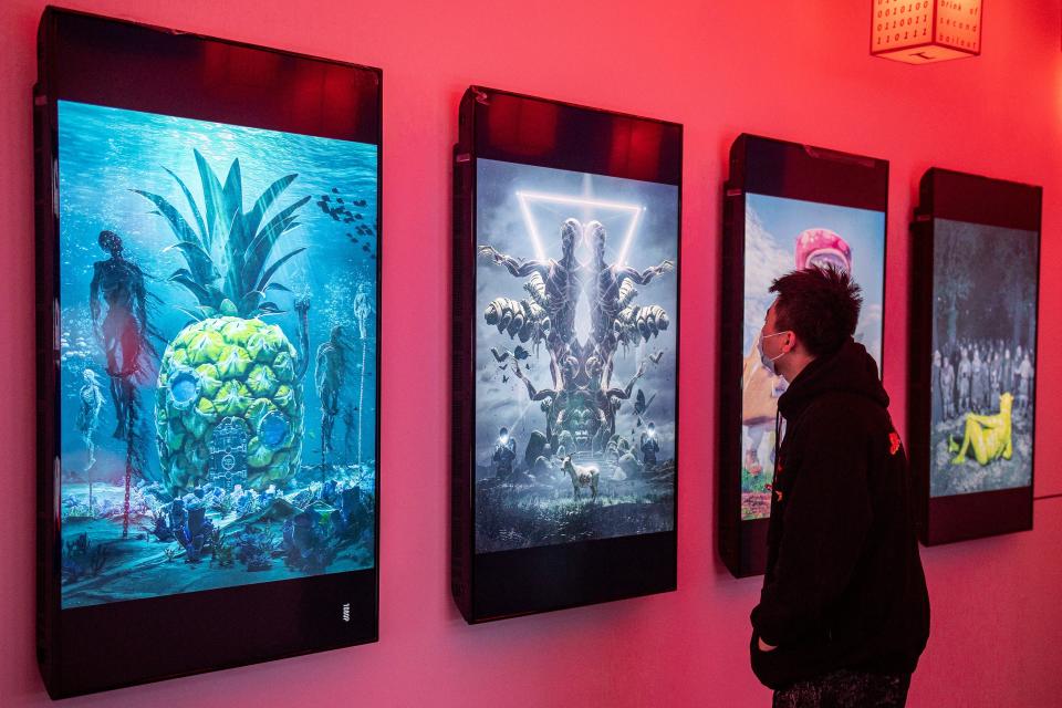 A man looks at digital paintings by US artist Beeple at a crypto art exhibition entitled Virtual Niche: Have You Ever Seen Memes in the Mirror?, one of the world's first physical museum shows of blockchain art, ahead of its opening in Beijing on March 26, 2021. - RESTRICTED TO EDITORIAL USE - MANDATORY MENTION OF THE ARTIST UPON PUBLICATION - TO ILLUSTRATE THE EVENT AS SPECIFIED IN THE CAPTION (Photo by NICOLAS ASFOURI / AFP) / RESTRICTED TO EDITORIAL USE - MANDATORY MENTION OF THE ARTIST UPON PUBLICATION - TO ILLUSTRATE THE EVENT AS SPECIFIED IN THE CAPTION / RESTRICTED TO EDITORIAL USE - MANDATORY MENTION OF THE ARTIST UPON PUBLICATION - TO ILLUSTRATE THE EVENT AS SPECIFIED IN THE CAPTION (Photo by NICOLAS ASFOURI/AFP via Getty Images)