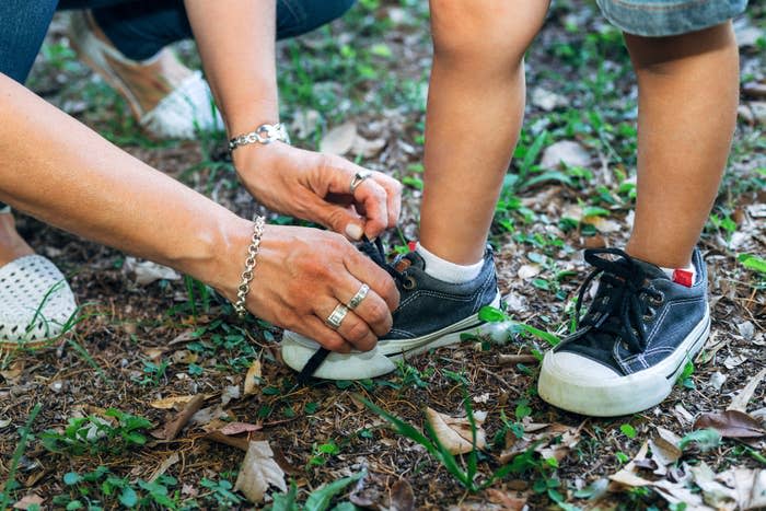 Adult helping child tie shoelaces on grass