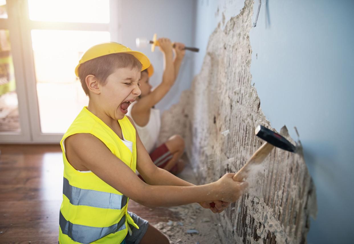 Two little manual workers renovating their room. Boys aged 7 are tearing out plaster from the walls using hammer and chisel.