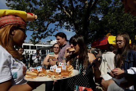 A woman gives away hot dogs from vendor Walter's on a platter during the opening of an exhibit at Ellis Island highlighting the immigrant history behind the "Hot Dog" in New York City, U.S., June 28, 2017. REUTERS/Lucas Jackson
