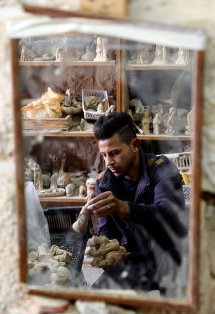 A Palestinian man is reflected in a mirror as he collects figurines for sale during Christmas season, at a workshop in Bethlehem in the occupied West Bank, December 10, 2018. REUTERS/Raneen Sawafta