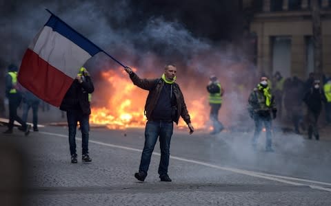 A protestor waves a French flag during clash with riot police amid tear gas near the Champs Elysees in Paris - Credit: LUCAS BARIOULET/AFP/Getty Images