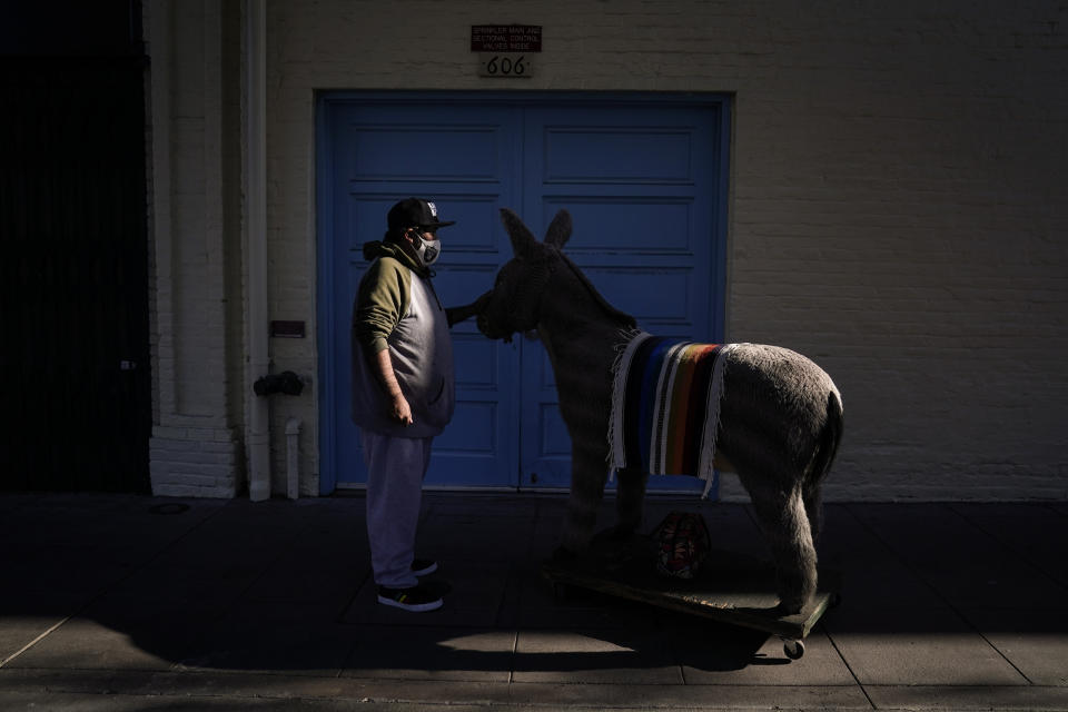 Jesus Hernandez, a merchant who owns a gift shop on Olvera Street that only opens on weekends due to the pandemic, waits for a key to store his uncle's life-size stuffed donkey, a photo prop named George, in downtown Los Angeles, Wednesday, Dec. 16, 2020. Olvera Street, known as the birthplace of Los Angeles, has been particularly hard hit by the coronavirus pandemic, with shops and restaurants closed and others barely hanging on. (AP Photo/Jae C. Hong)