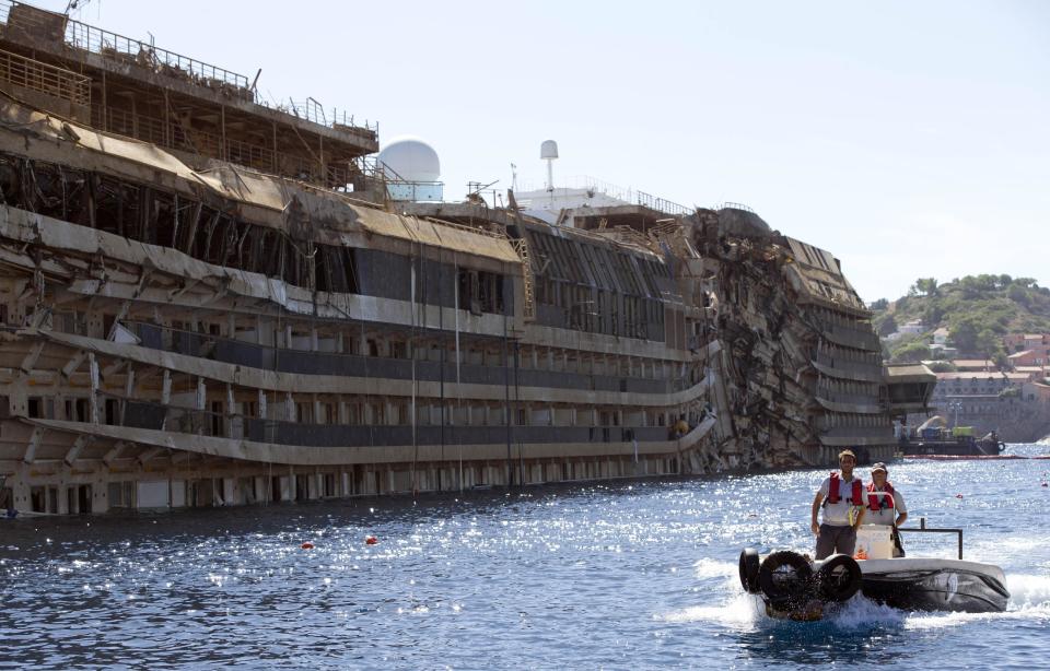 FILE - In this Sept. 18, 2013 file photo, a small boat navigates past the damaged side of the Costa Concordia ship after it was pulled upright, on the Tuscan Island of Giglio, Italy. Divers searching the submerged part of the wreck of the cruise ship have found the remains of one of the two people still missing from the 2012 disaster. Officials believe the remains belong to Russel Rebello, an Indian waiter. Thirty-two people died when the Concordia slammed into a reef off the Tuscan island of Giglio and capsized on Jan. 13, 2012. (AP Photo/Andrew Medichini, file)