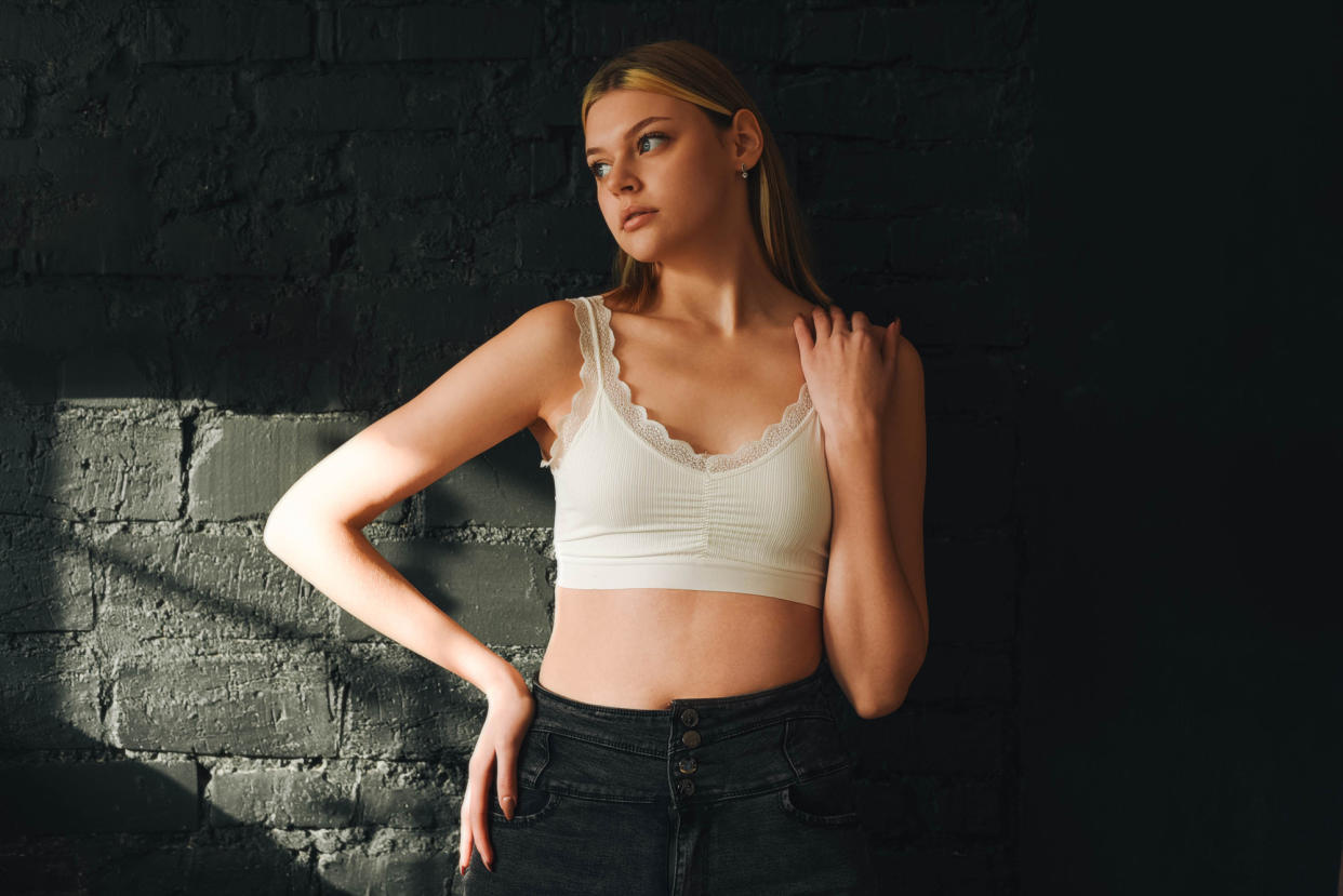 Portrait of a beautiful girl in a white top against a dark wall. Beautiful girl. Blonde. White top. Natural makeup.