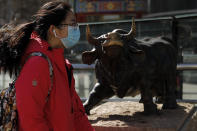 A woman wearing a protective face mask walks by the investment icon bull statue on display outside a bank in Beijing, Tuesday, March 10, 2020. Asian stock markets took a breather from recent steep declines on Tuesday, with several regional benchmarks gaining more than 1% after New York futures reversed on news that President Donald Trump plans to ask Congress for a tax cut and other quick measures to ease the pain of the virus outbreak. (AP Photo/Andy Wong)