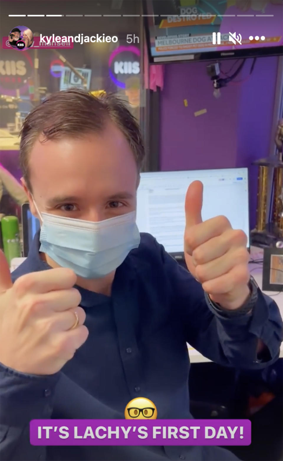 Beauty and the Geek star Lachy Mansell wears a face mask and gives a thumbs up from his desk at his new job on KIIS FM's The Kyle & Jackie O Show