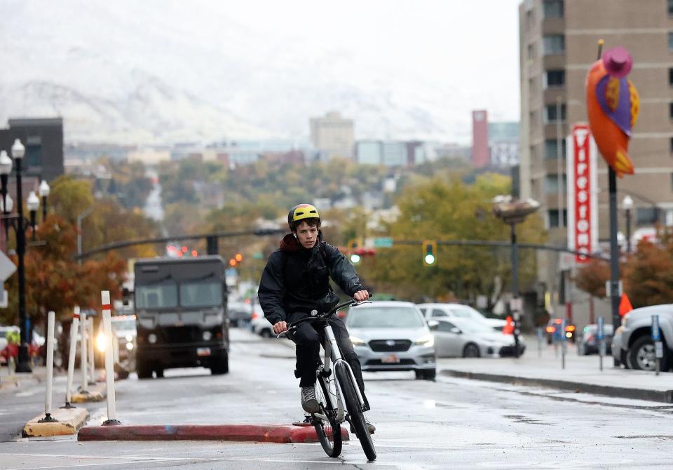 Kai Casperson bikes through downtown Salt Lake City as snow dusts the mountains on Thursday, Oct. 26, 2023. | Kristin Murphy, Deseret News