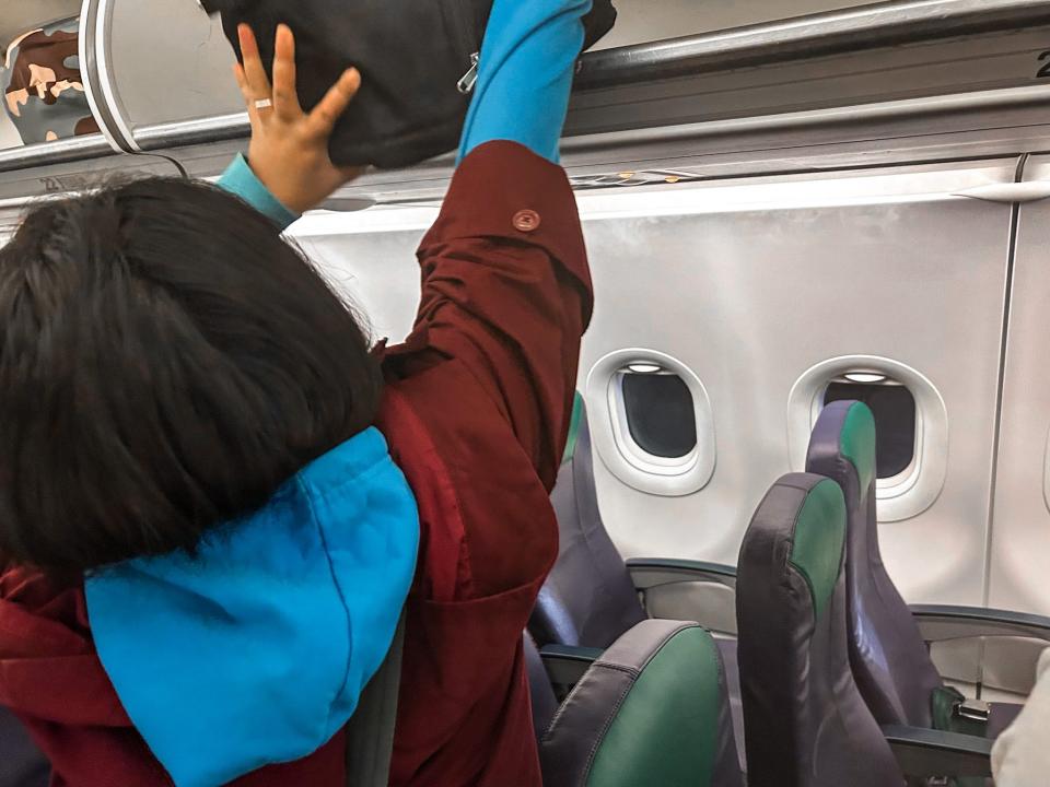 A person putting their beg in the overhead compartment.