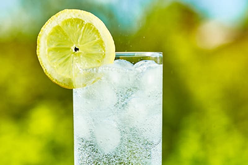 Sparkling water and lemon slice on glass with an ice, sunny day - narrow focus on middle of the glass