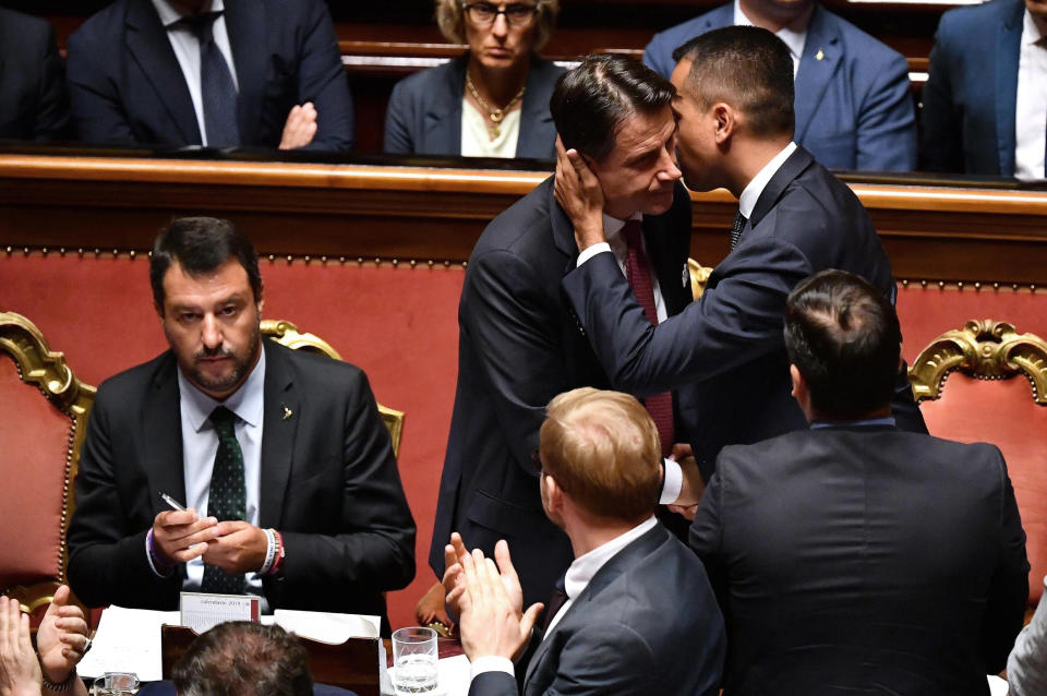 Italian Premier Giuseppe Conte, center, is hugged by Deputy Premier Luigi Di Maio at the end of his address to the Senate as the League's Matteo Salvini sits at left, in Rome, Tuesday, Aug. 20, 2019. Conte on Tuesday announced his resignation, blaming his decision to end his 14-month-old populist government on his rebellious and ambitious deputy prime minister Matteo Salvini. (Ettore Ferrari/ANSA via AP)