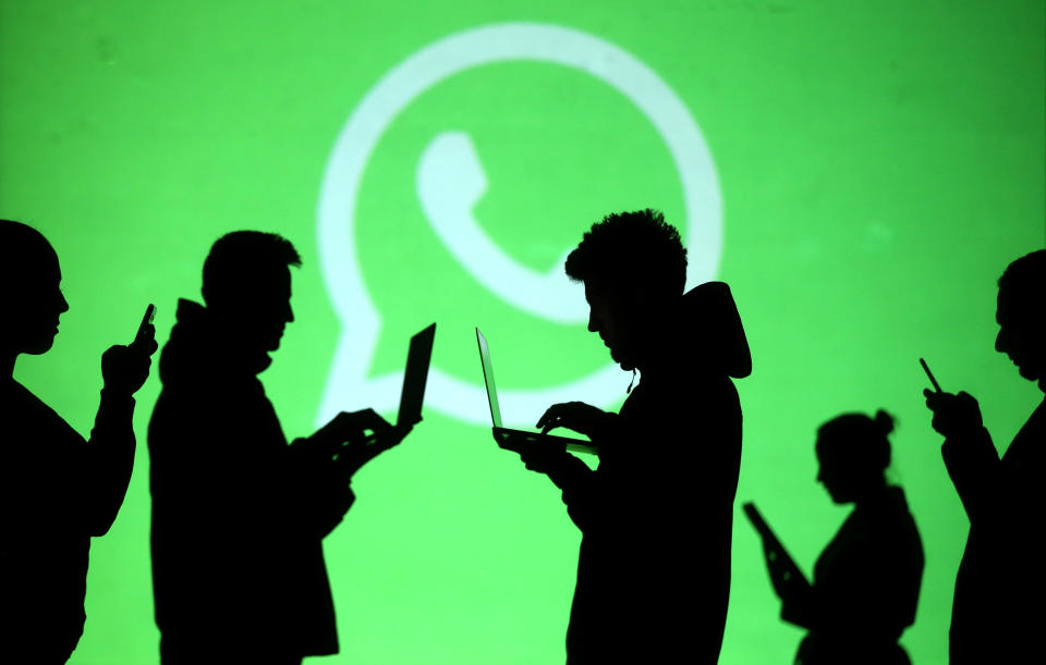 Silhouettes of laptop and mobile device users are seen next to a screen projection of Whatsapp logo in this picture illustration taken March 28, 2018.  REUTERS/Dado Ruvic/Illustration